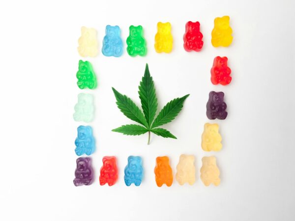 Caramelle al THC che circondano una foglia di cannabis su sfondo bianco