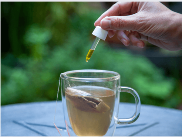 une main qui met de l'huile de CBD dans un tisane